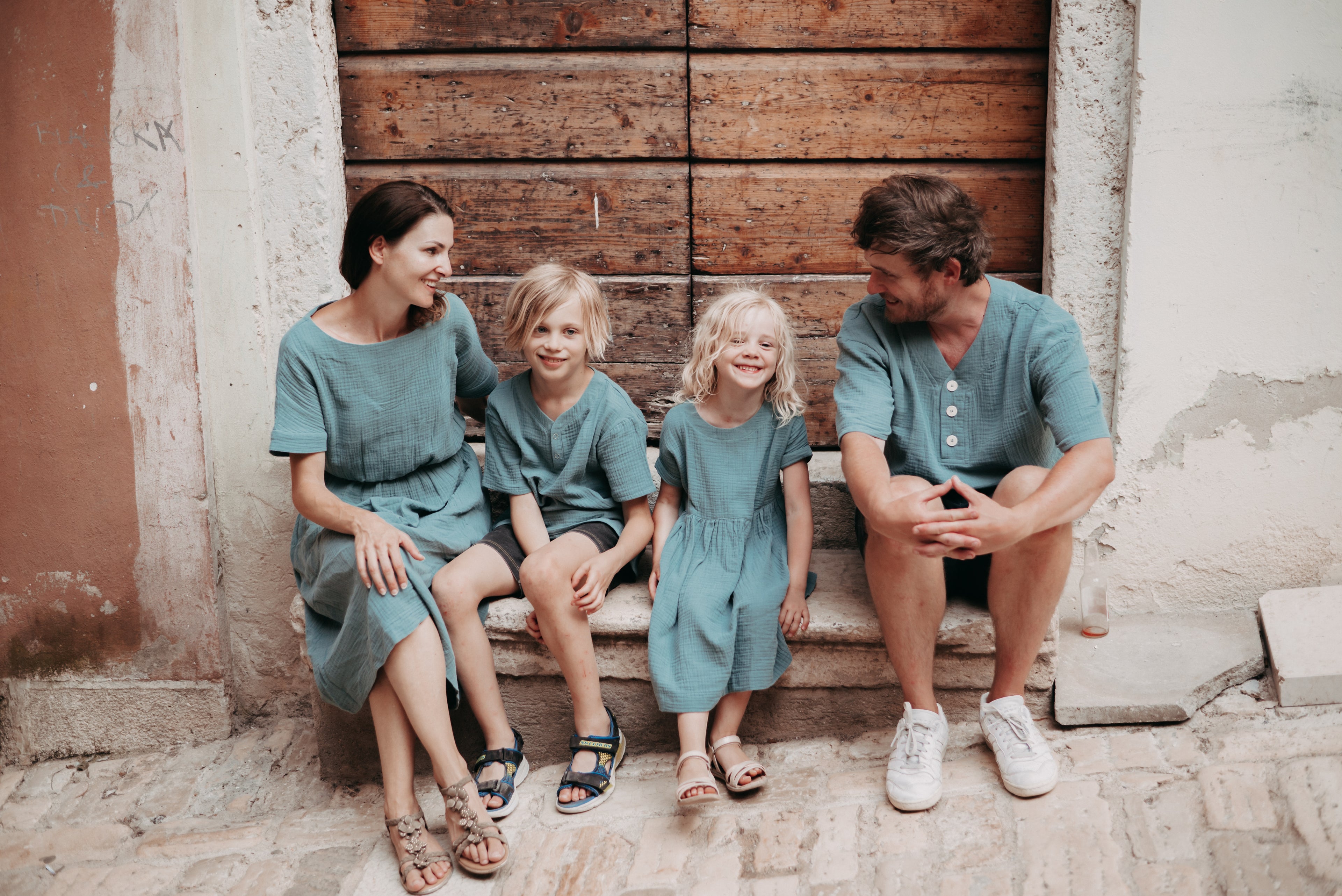 Familie im Partnerlook aus Musselin vor einem Holztor, Mini Me Outfits, Matching Outfits für die ganze Familie, Mutter mit Kindern, Vater mit Kindern