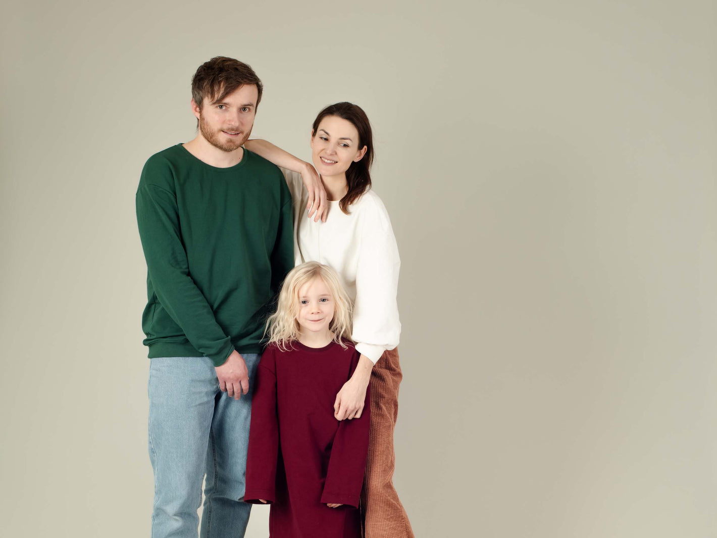 Familie in Pullis in Weihnachtsfarben (Rot, Grün, Weiß) steht zusammen und sieht in die Kamera